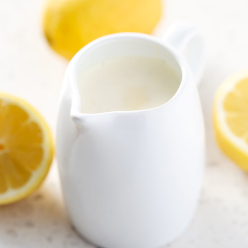 small pitcher of salad dressing with lemons on white background