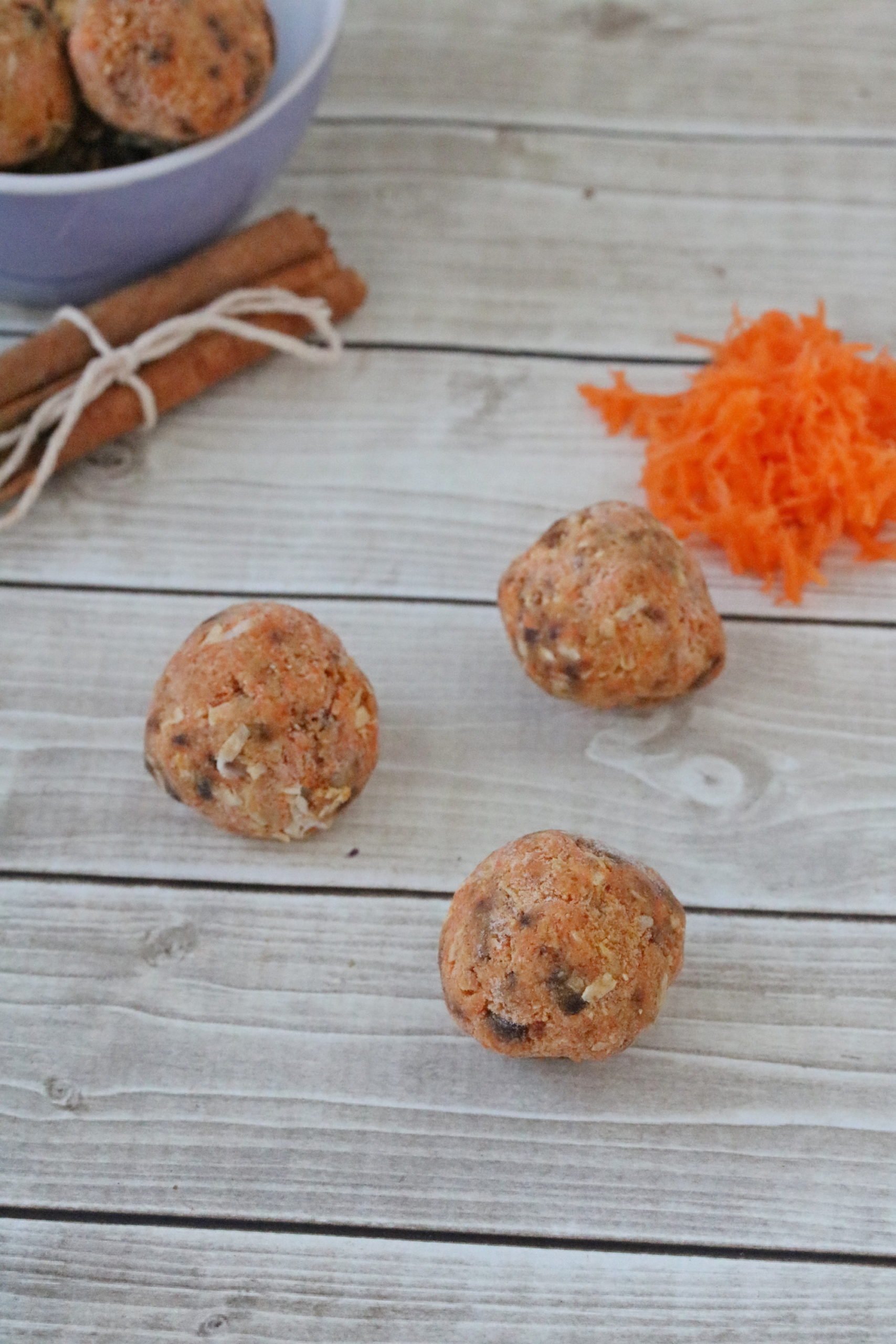 Carrot cake energy balls with shredded carrot and cinnamon behind them