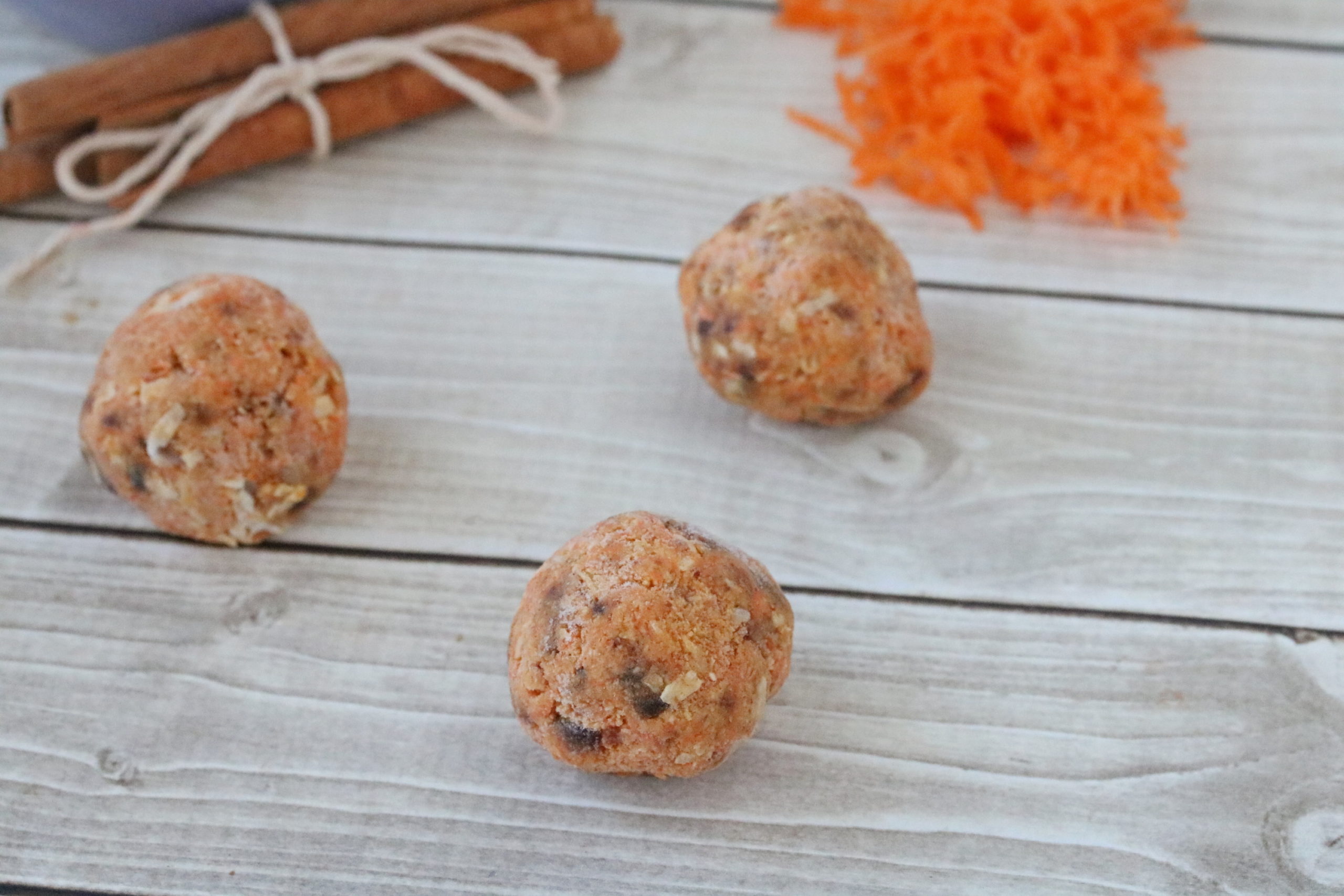 Carrot cake energy balls with shredded carrot and cinnamon behind them