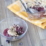 Easy berry crumble in cooking pan with a spoonful missing and a serving spoon in the pan on a yellow napkin