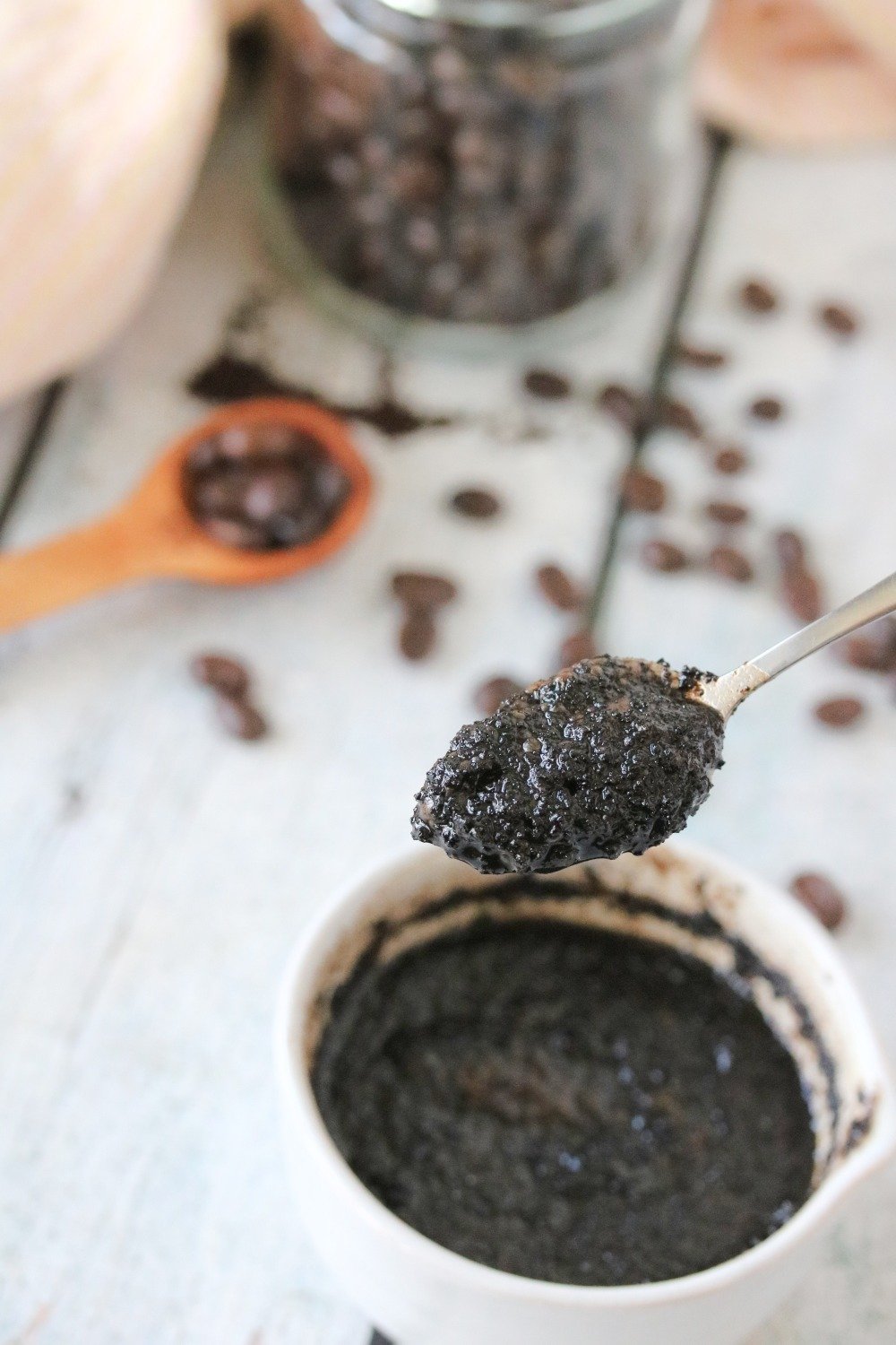 DIY coffee face scrub in a white bowl with coffee beans behind it