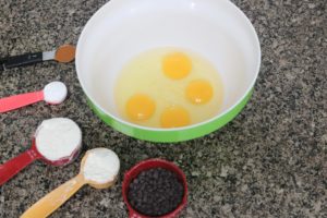 In process image for chocolate chip zucchini muffins: eggs in a green bowl with ingredients lined up