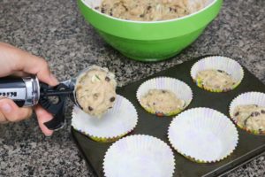 In process image for chocolate chip zucchini muffins: portioning out muffin mixture with an ice cream scoop into a muffin tin
