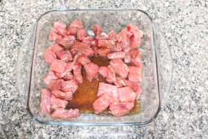 Chunks of raw beef in a glass dish marinating