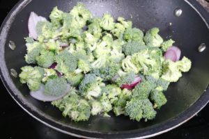 Chopped broccoli and red onion in a black wok on the stove