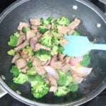 Chunks of beef and broccoli cooking in a black wok with a blue spatula in it
