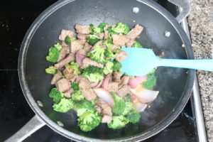 Chunks of beef and broccoli cooking in a black wok with a blue spatula in it